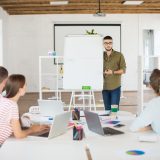 young-man-eyeglasses-shirt-standing-near-white-board-while-thoughtfully-discussing-new-project-with-colleagues-group-creative-people-working-together-modern-white-office (1)